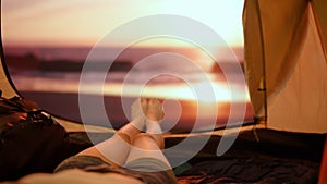 Person on campsite traveling and hiking, exploring nature. Young woman lying inside the tent at sunset on the beach