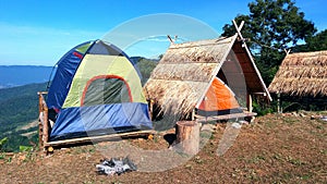 The camping blue/Green and orange tent on wooden litter with dry leaves roof and blue sky, mountain and tree