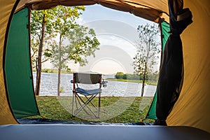 Camping chair in front of the tent, green grass ground of camping ground near the lake, holiday activities