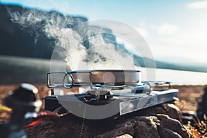 Camping cooking in nature outdoor, prepare breakfast picnic in mist morning; cooker food metal gas stove on stone; tourism