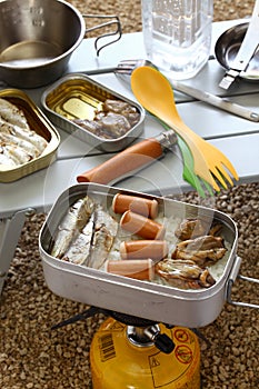 Camping cooking. oiled sardines, sausages and smoked oysters on boiled rice in mess tin.