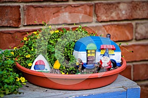 Camping gnome fairy garden in planter with minature camper and tent against blurred brick wall