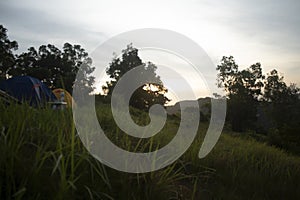 Camping on hills. Sunrise sunset in the mountains. Rural view background of country side with green grass and warm sun light.