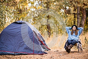 Camping holiday, tourist traveler woman in sweater and black hat ralaxing in camp tent in forest, rest vacation concept
