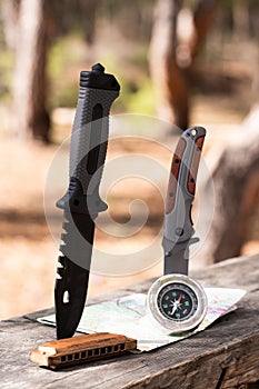 Camping knife, compass and map on a wooden table in the forest.