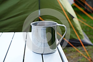 Camping metal mug on table with green tent in bcakground