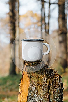Campeggio metallo bianco tazza deridere su piedi sul un albero tronco d'albero foresta al di fuori. smaltato vuoto tazza vuoto spazio 