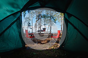 Camping in the middle of the forest, taken from inside the tent. View of the folding table and chairs with gas stove in the backgr