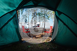 Camping in the middle of the forest, taken from inside the tent. View of the folding table and chairs with gas stove in the backgr