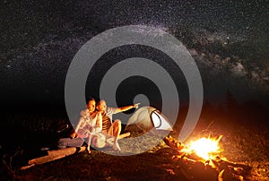 Tourist family with daughter having a rest in mountains at night under starry sky with Milky way