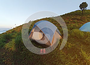 Camping on the mountains. A tourist tent on a green hill. A pink shoe in front of the tent.