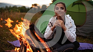 The girl is warming herself by the fire, smiling and looking to the camera