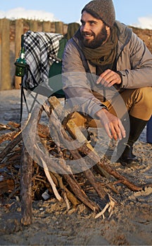 Camping out on the beach. A young man building a fire on the beach.