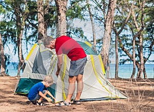 Camping people outdoor lifestyle tourists put up set up green grey camp site summer forest near lazur sea. Boy son helps photo