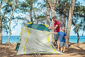 Camping people outdoor lifestyle tourists put up set up green grey campsite summer forest near lazur sea. Boy son helps photo