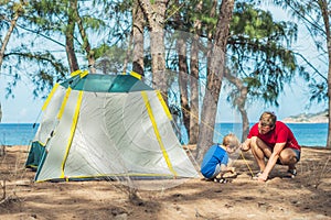 Camping people outdoor lifestyle tourists put up set up green grey campsite summer forest near lazur sea. Boy son helps