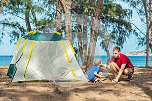 Camping people outdoor lifestyle tourists put up set up green grey campsite summer forest near lazur sea. Boy son helps