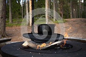 Camping pot over burning campfire. Bowler hat on a fire on the background