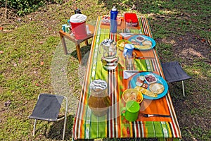 Camping stools and picnic table in the forest camping site with water, juice, vegetables, fruit salad, omelet and toast