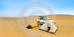 Camping in the Sudanese desert with two small tents, an off-road vehicle and a sand dune in the background