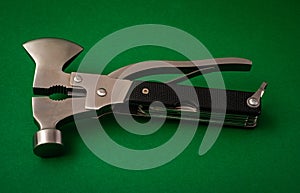 Camping or survival multi tool , with axe hammer and pliers on green background