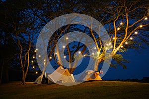 camping tent on grass courtyard and warm night light under dark blue sky. Family vacation picnic on holiday relax