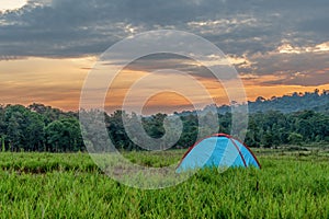 Camping tent on grass field with background of forest and mountains and sunrising sky in natural park