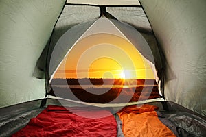 Camping tent with sleeping bags near river at sunset