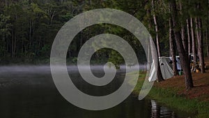 Camping tents in forest near mist lake. Peoples relax on nature