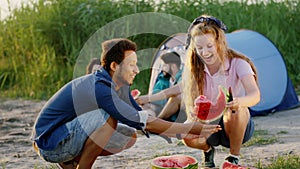 Camping time multiethnic group of friends cut a big watermelon into pieces and enjoying the time at nature and sunset