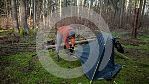 Camping, tourism and travel concept. Man setting up tent outdoors. Hiker assembles campsite tent in the autumnal forest