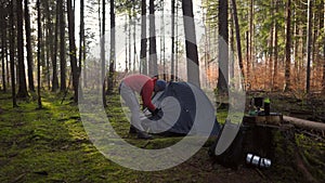 Camping, tourism and travel concept. Man setting up tent outdoors. Hiker assembles campsite tent in the autumnal forest