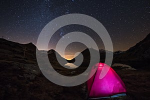 Camping under starry sky and Milky Way arc at high altitude on the italian french Alps. Glowing tent in the foreground. Adventure