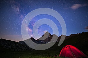 Camping under starry sky and milky way at high altitude on the Alps. Illuminated tent in the foreground and majestic mountain peak