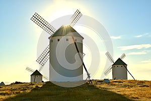 Campo de Criptana windmills illuminated by the sun in the background.