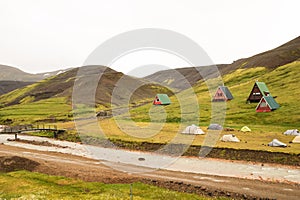 Campsite with cabins and tents in volcanic mountains in geothermal area in Kerlingarfjoll near route f35 in Iceland, green grass