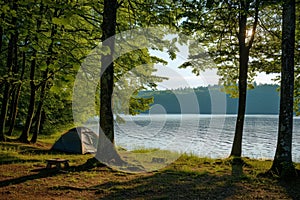Campsite with a tent set up in the woods near a tranquil lake, A peaceful lakeside campsite with a view of the water
