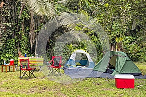 Campsite in tropical forest with two tents, chairs, table, food and drinks and cooler