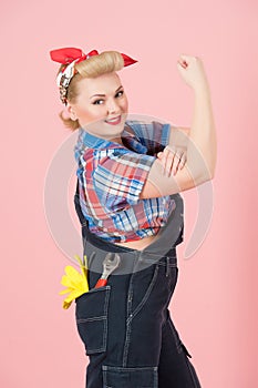 We Can Do It concept with blonde curls girl on pink background. Blonde Cute Girl repairer with hand up.