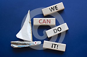 We can do it symbol. Concept words We can do it on wooden blocks. Beautiful deep blue background with boat. Business and We can do