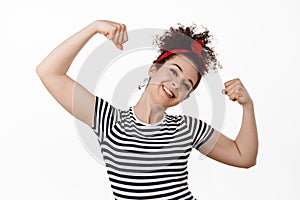 We can do it. Women rights. Strong and confident brunette girl flex biceps, smiling and showing strong hands, arm