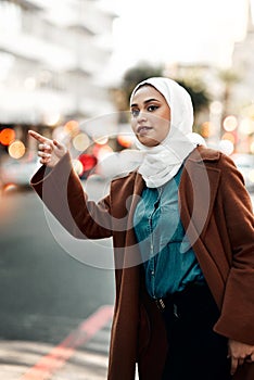 Can I get a taxi please. an attractive young woman wearing a hijab and hailing a taxi in the city.