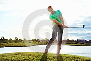 He can make that shot from a mile away. a man practicing his swing on the golf course.