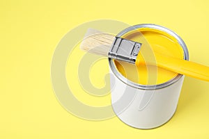 Can of paint with brush on pale yellow background, closeup. Space for text