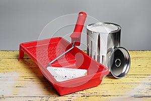 Can of paint and tray with roller on yellow wooden table