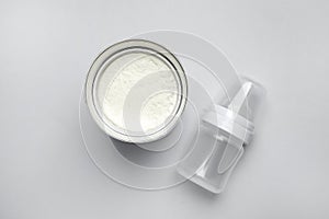 Can of powdered infant formula with feeding bottle on light background, flat lay. Baby milk