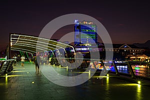 Can Tho city lights night skyline pedestrian bridge on river, blurred motion people walking on waterfront promenade, Mekong Delta