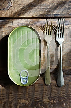 Can with two forks on a wooden table. Tinned fish concept. Rustic style.