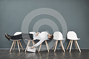 Can this wait get any longer. a young man lying down on a row of chairs while waiting in line for a job interview.