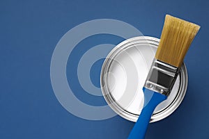 Can with white paint and brush on blue background, top view. Space for text